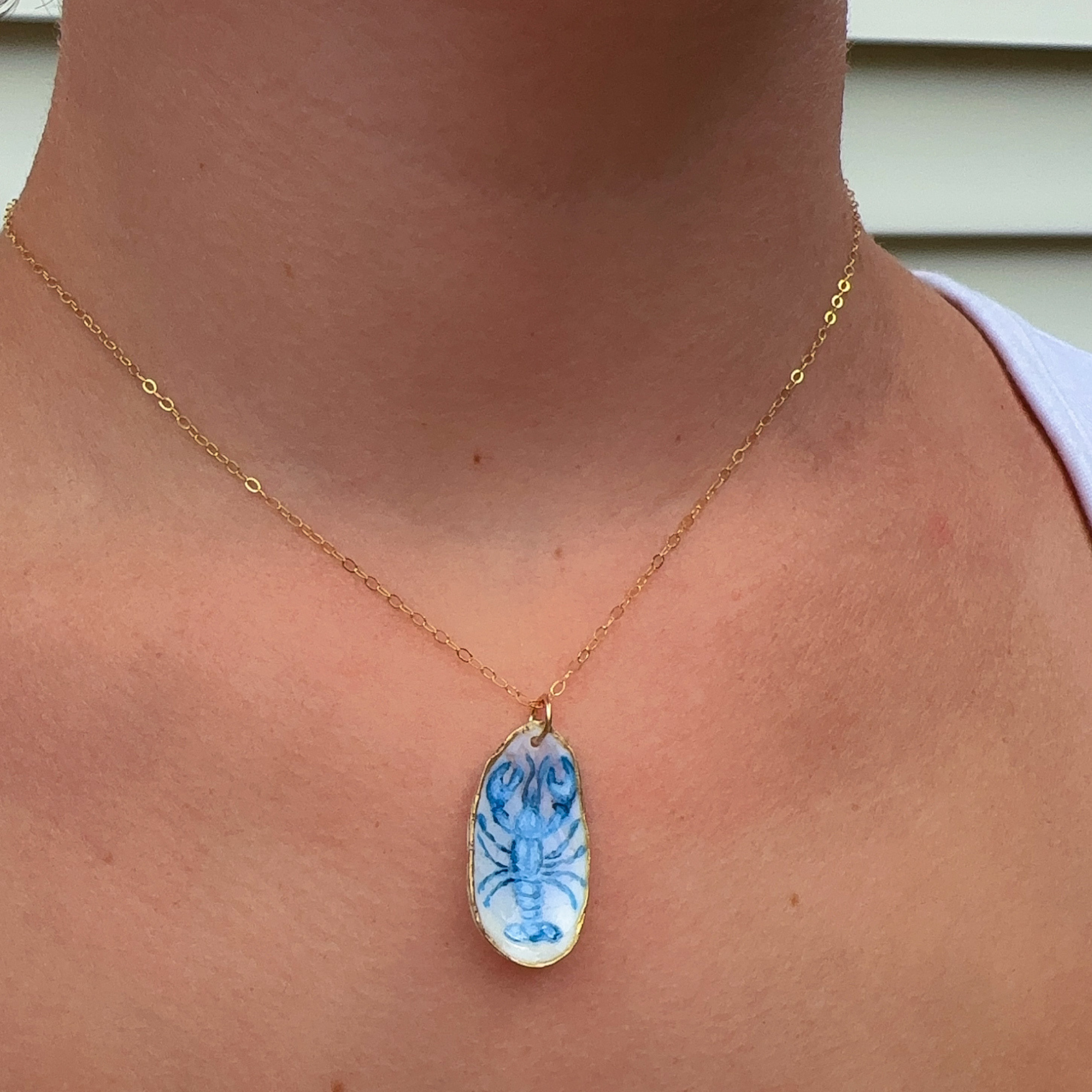 Close-up of hand-painted blue lobster design on a coastal oyster shell necklace pendant