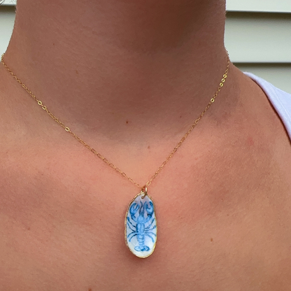 Close-up of hand-painted blue lobster design on a coastal oyster shell necklace pendant